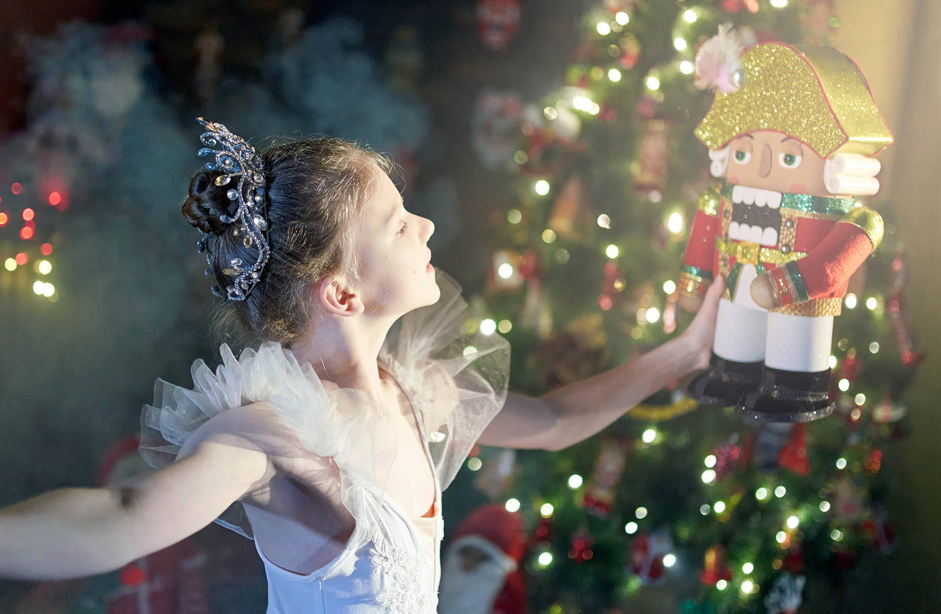 Cute pre-adolescence girl ballet dancer is standing in a ballet pose. She is holding the Nutcracker toy in her hands. Shooting in a living room with Christmas decor