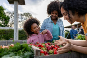 Happy African American girl shopping at the Farmer's Market with her mother and wanting to try the strawberries
